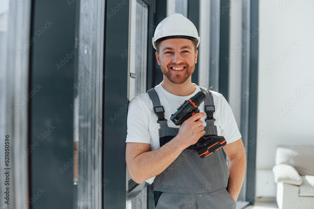 Using drill by installing windows. Repairman is working indoors in the modern room Using drill by installing windows. Repairman is working indoors in the modern room