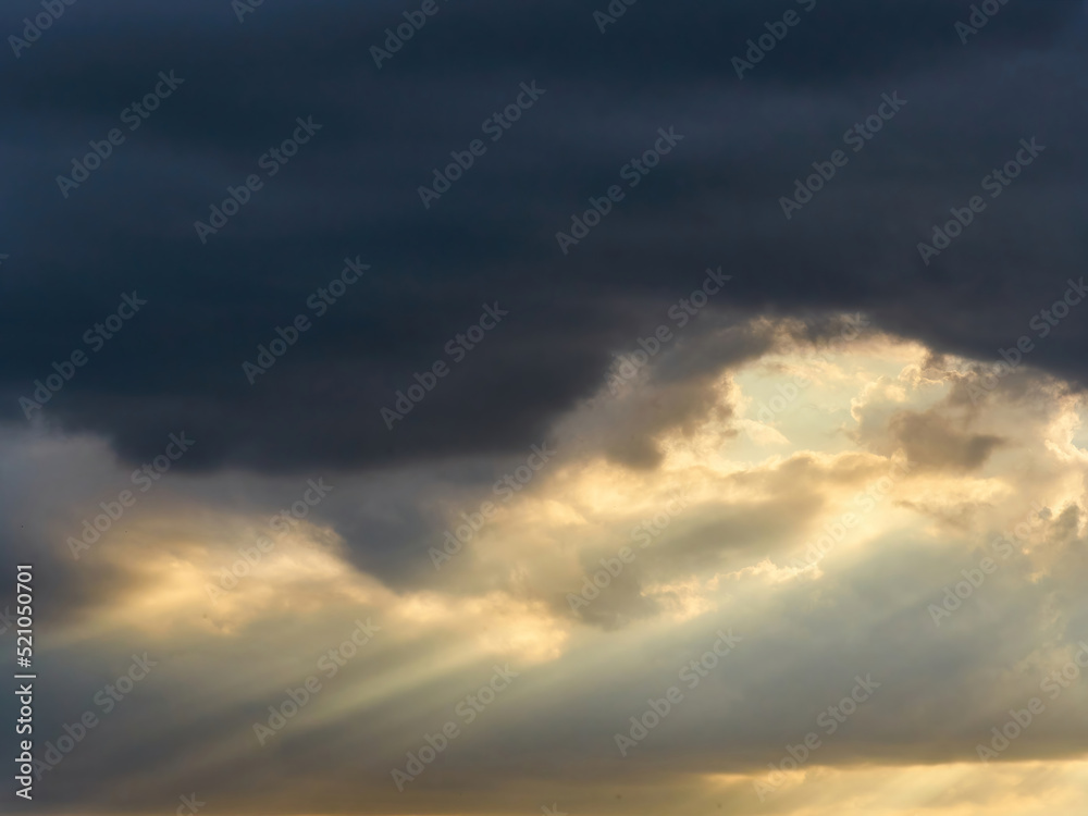 Skyscape with sunlight bursting through the leaden gloom of heavy storm clouds.