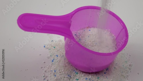 Pouring detergent powder into a pink plastic measuring scoop for laundry powder on a white background photo