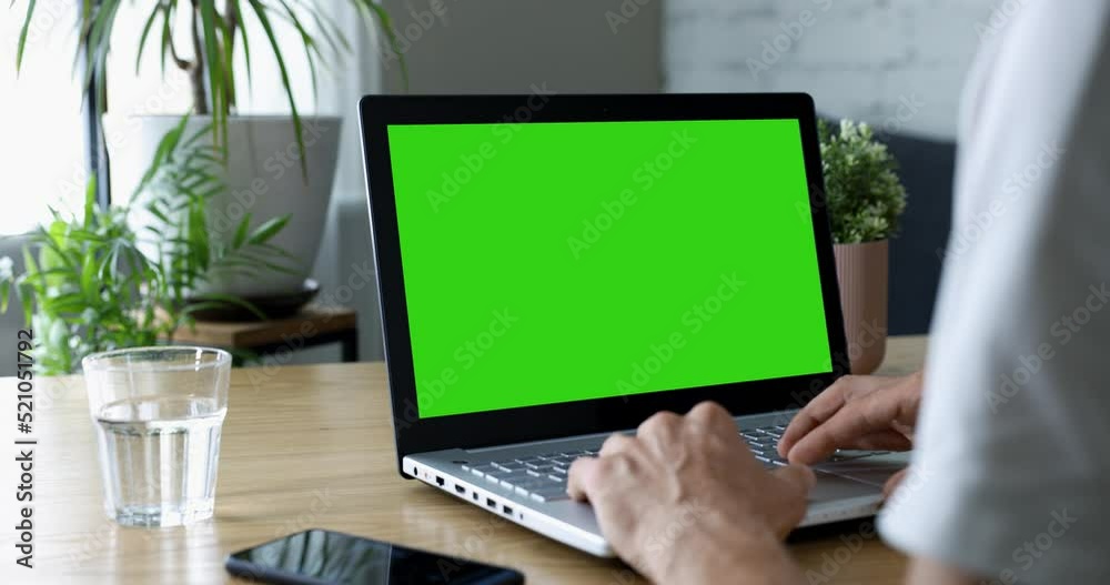 man sitting at desk and using laptop computer at home. scrolling the website. mockup with blank green screen