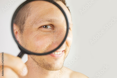 man with magnifying glass near eye mimic wrinkles on face. Portrait isolated on white. Clean healthy skin and cosmetology concept. Image for cosmetology clinic advertising.