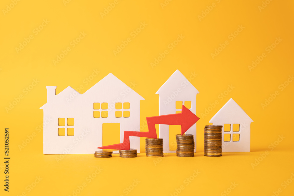 Coins on a table, a red up arrow and house. The concept of the rising price of real estate Coins on a table, a red up arrow and house. The concept of the rising price of real estate
