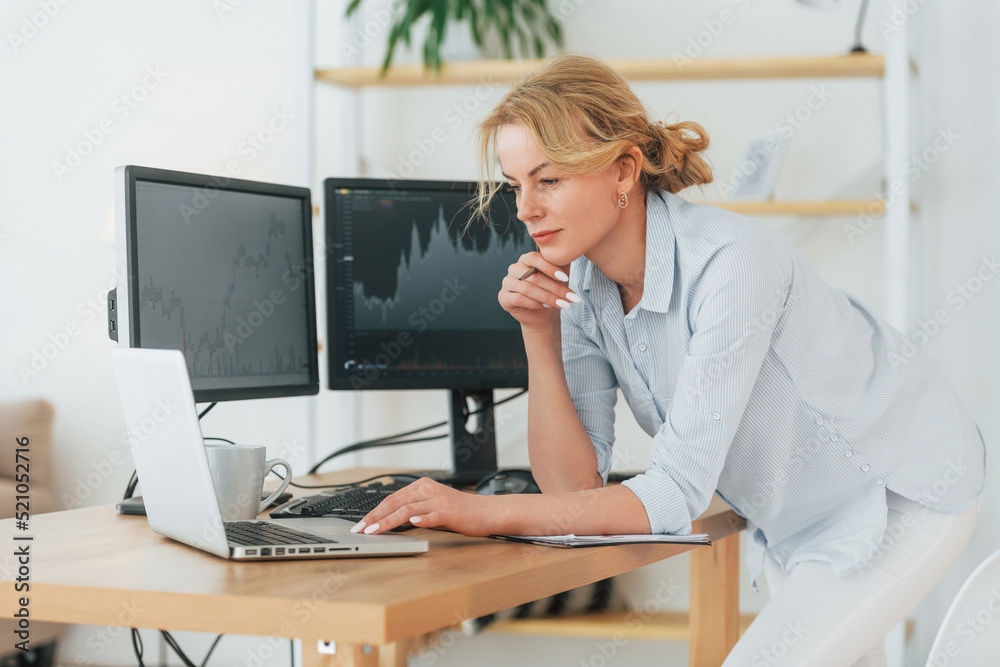 Standing and using laptop. Female stock broker in formal wear is working in the office Standing and using laptop. Female stock broker in formal wear is working in the office