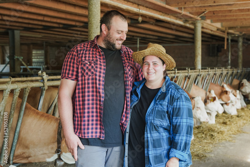 Happy farmer couple smiling on camera while hugging each other inside cowshed