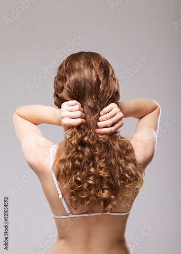 a woman with long, well-groomed curly hair stands with her back to the camera straightening them with her hands