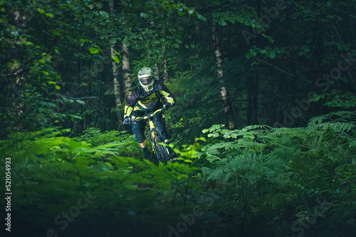 Man, cyclist in the full face helmet fast rides on the yellow enduro bicycle in the green forest