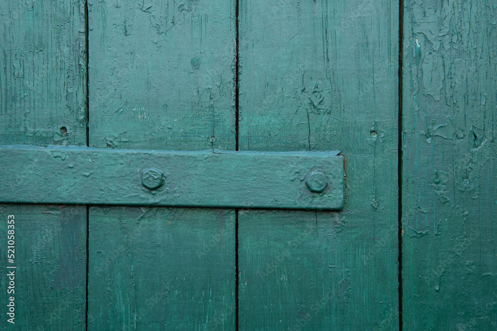 Vertical wooden planks with the horizontal metal element are covered in green paint. Close-up view. Wooden vintage background. Vertical wooden planks with the horizontal metal element are covered in green paint. Close-up view. Wooden vintage background.