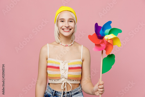 Young smiling happy blond lesbian woman 20s she wear colorful knitted top yellow hat holding toy windmill fooling around isolated on plain pastel light pink background. People lgbtq lifestyle concept. photo