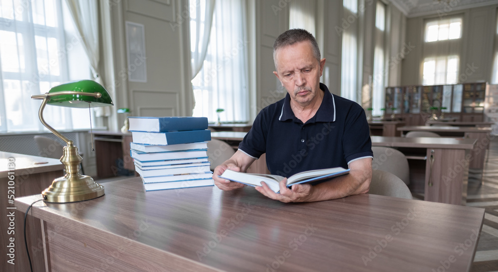 Portrait of caucasian Senior man working with book in public library. Adult student at the library, he is sitting at desk and reading a book. learning and education concept Portrait of caucasian Senior man working with book in public library. Adult student at the library, he is sitting at desk and reading a book. learning and education concept