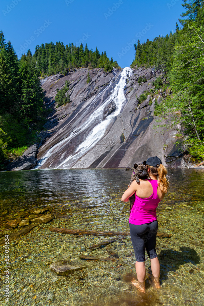 Adventurous athletic female hiker standing at the base of a waterfall in the Pacific Northwest with her French Bulldog.