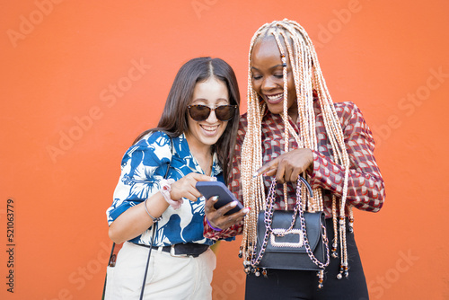 Ritratto di due giovane ragazze che guardano lo Smartphone in tutta felicita isolate sullo sfondo arancione  photo