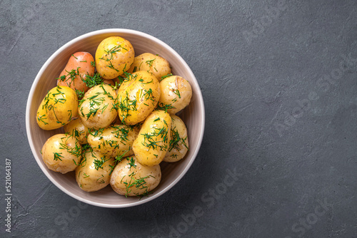 Boiled unpeeled potatoes with fresh dill and oil on a graphite background. Side view, copy space