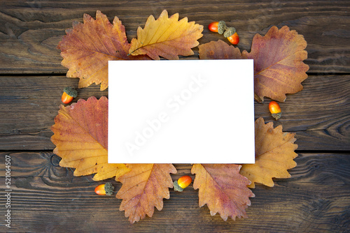 Background of autumn oak leaves and acorns on wooden boards with copy space. White card for text. Leaf texture, wood texture.