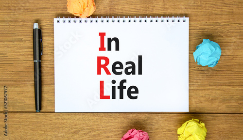 IRL in real life symbol. Concept words IRL in real life on white note on a beautiful wooden background. Metallic pen. Business and IRL in real life concept. Copy space. © Dzmitry