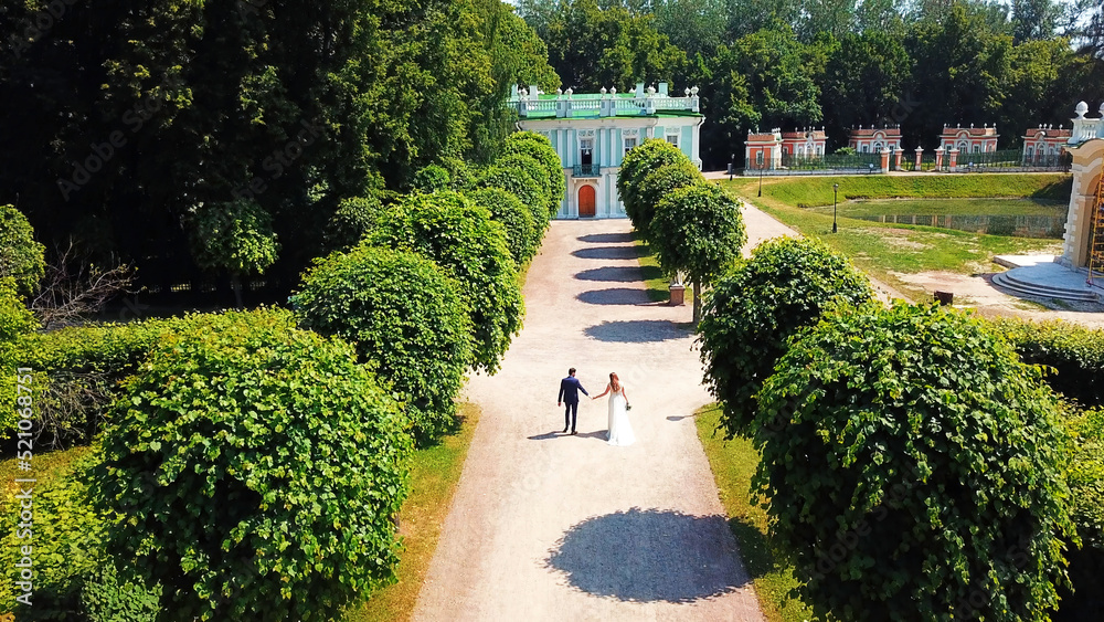 The view from the drone.Creative.A beautiful summer park with small beautifully trimmed trees and a summer road on which beautiful buildings and museums are visible and there is a young married couple