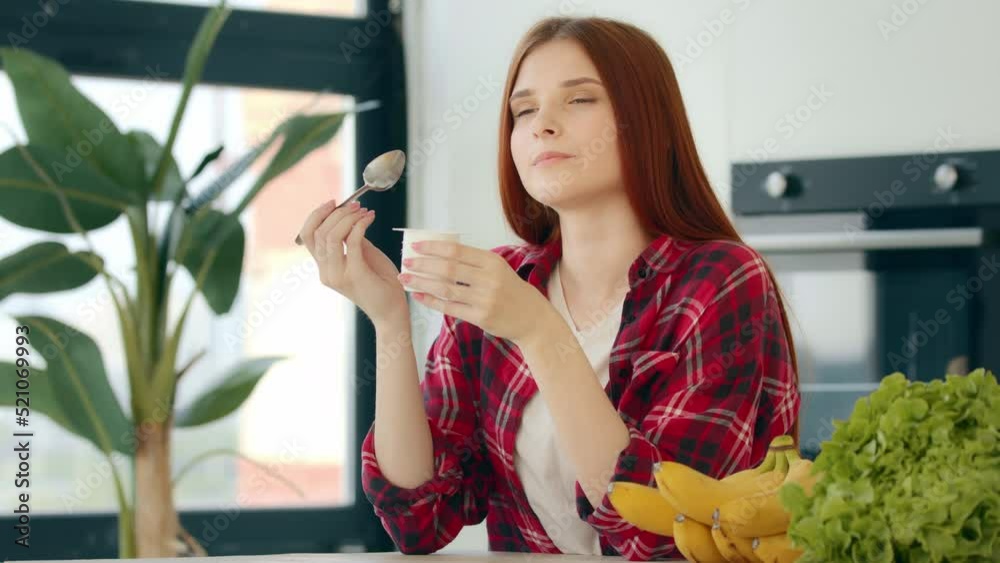 Domestic young woman housewife redhead female eating yogurt with fresh fruits tasting natural milk product dairy dessert use spoon at kitchen enjoying morning breakfast keeping diet healthy nutrition Domestic young woman housewife redhead female eating yogurt with fresh fruits tasting natural milk product dairy dessert use spoon at kitchen enjoying morning breakfast keeping diet healthy nutrition