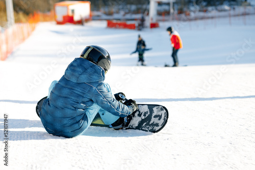 snowboarder checking equipment on a ski slope, snow and bright daylight