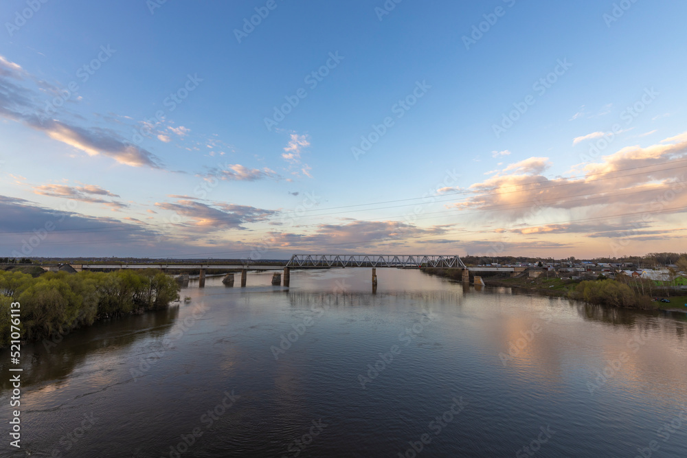 Fototapeta premium Evening landscape, sunset on the river. View of the industrial area of the railway bridge. Outskirts.