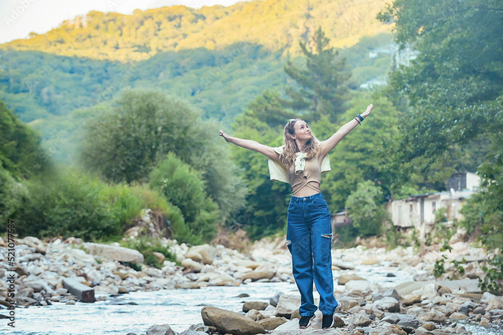 a beautiful tourist girl enjoys life near a mountain river on the rocks, in the background she has mountains