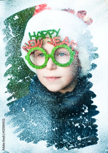 Fototapeta Naklejka Na Ścianę i Meble -  little boy in santa claus costume looking throught the snowy window