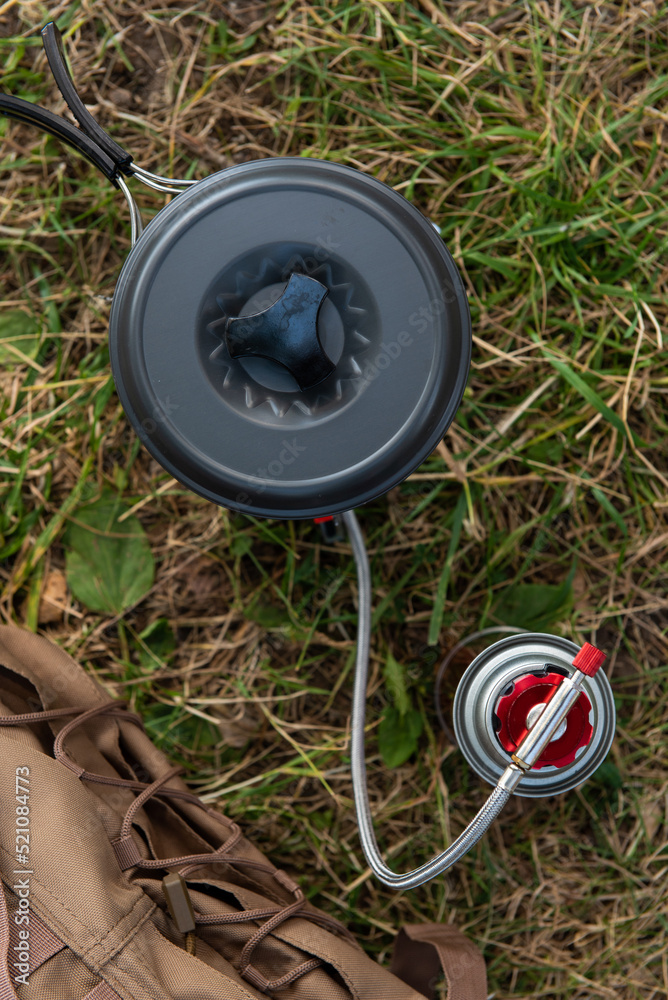 Naklejka premium tourist gas burner with a tourist pan working installed on the ground against the background of green grass