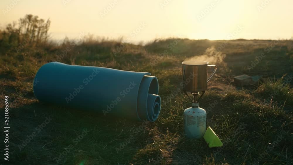 Close-up of a road gas burner and a small mug of boiling water at dawn Close-up of a road gas burner and a small mug of boiling water at dawn