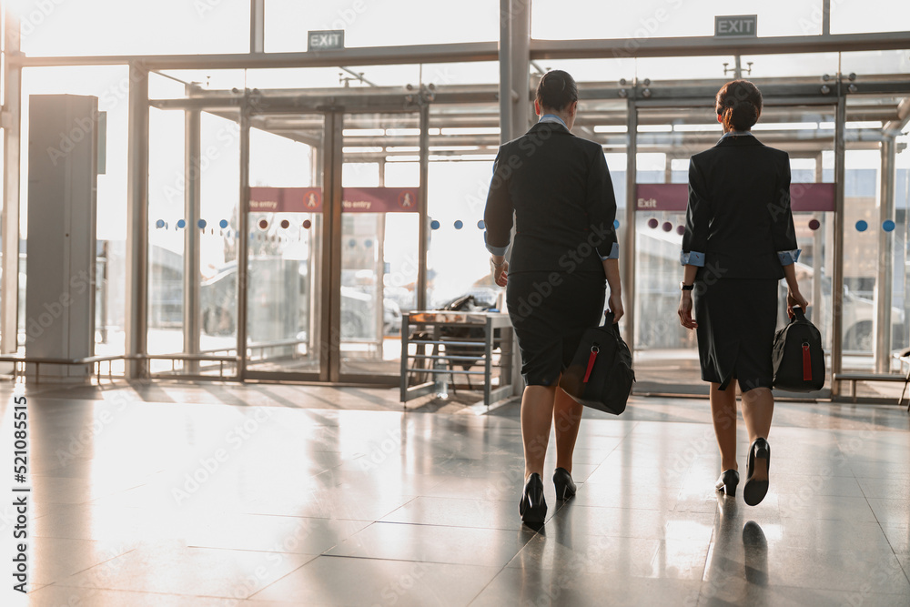 Fototapeta premium Two flight attendants holding bags and walking in the airport