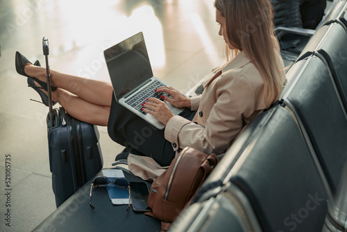Woman typing on laptop while putting her feet on the suitcase in the airport