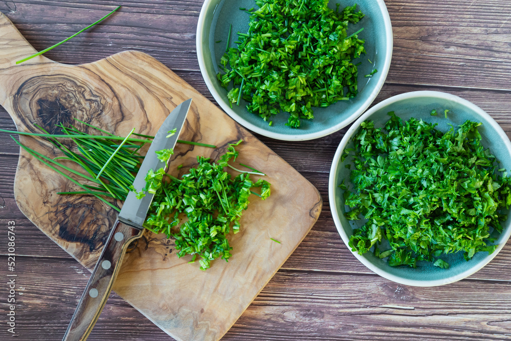 Fresh and chopped spicy parsley and chives herbs on cutting board, top view. - obrazy, fototapety, plakaty 