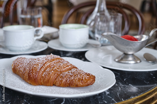 Crispy croissant on a white plate on a table in a cafe. Fresh homemade cakes. Delicious traditional french crispy croissants for breakfast 