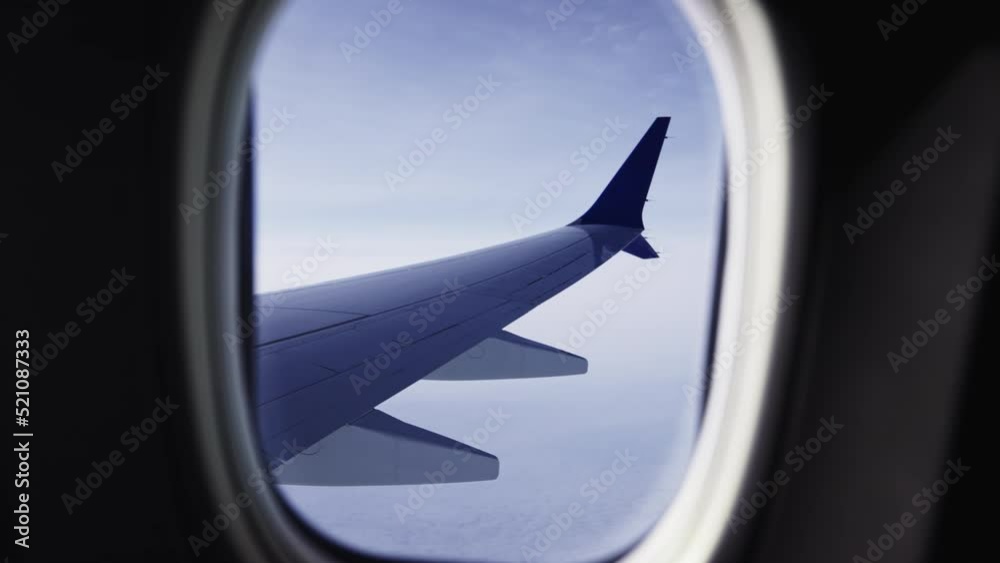 View Through Plane Window on an Aircrafts Wing and White Clouds Underneath View Through Plane Window on an Aircrafts Wing and White Clouds Underneath