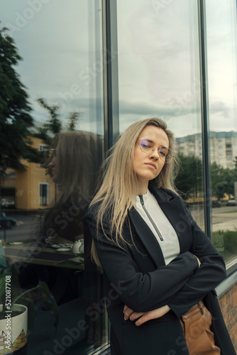 A beautiful woman in glasses stands leaning against the window of a building, looking into the camera. Free Download A beautiful woman in glasses stands leaning against the window of a building, looking into the camera. - GFXLoad