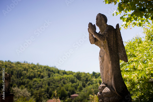 Statue of a praying angel outside Santa Maria and San Giorgio church in Fortunago, one of the most charming villages of Oltrepò Pavese, Lombardia countryside, Italy. Background with copy space. © silvia