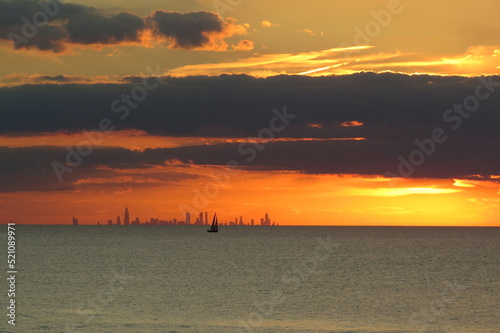 sunset glow over lake with city skyline and sailboat