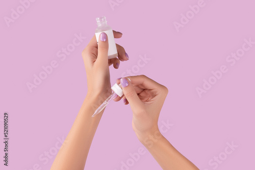 Womans hand holding dropper with serum on pastel lavender background © Darya Lavinskaya
