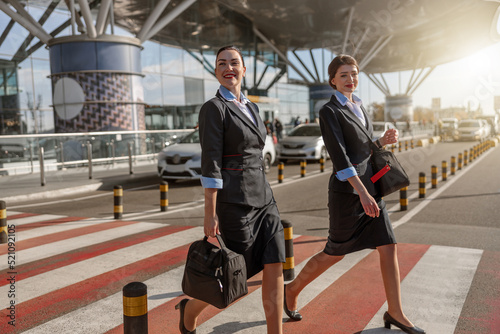 Two young stewardesses with bags crossing the road near terminal