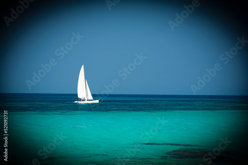 small white catamaran with a white sail. Blue skies and crystal clear waters. Tropical paradise concept. black vignette around the edges spyglass concept