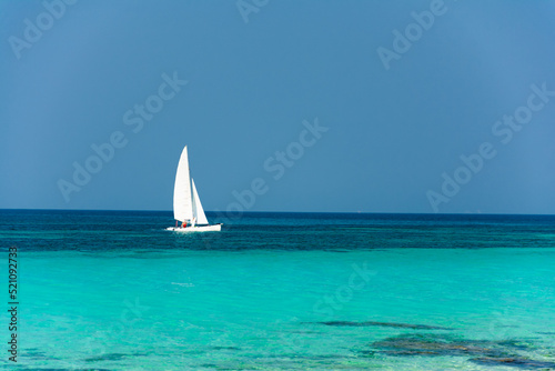 small white catamaran with a white sail. Blue skies and crystal clear waters. Tropical paradise concept
