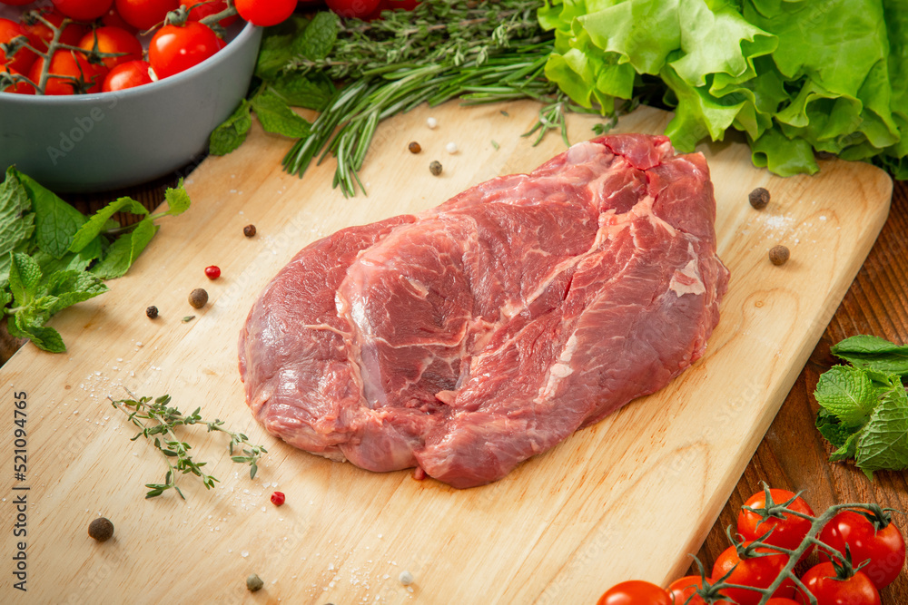 Beef neck tenderloin on a wooden cutting board with tomatoes and herbs around Beef neck tenderloin on a wooden cutting board with tomatoes and herbs around