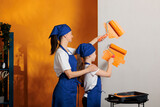 Mother and girl painting orange walls, using dye color to redecorate apartment room. Happy family doing housework renovation with paintbrush to paint home, having fun with decoration.