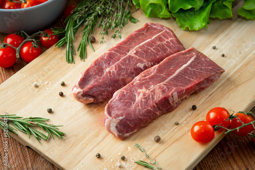 Top Blade steak on a wooden cutting board with tomatoes and herbs around