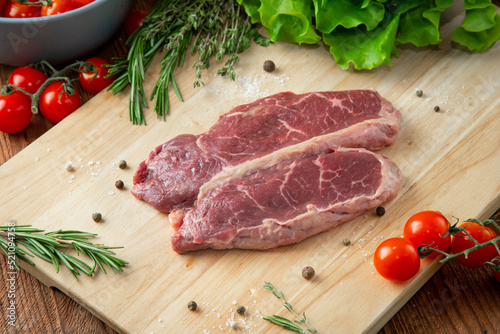 Picanha steak on a wooden cutting board with tomatoes and herbs around