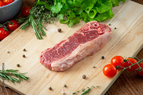 Striploin steak on a wooden cutting board with tomatoes and herbs around