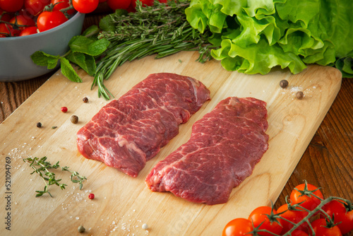 Denver steak on a wooden cutting board with tomatoes and herbs around