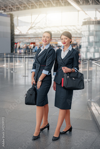 Smiling stewardesses with hand luggage standing in airport terminal