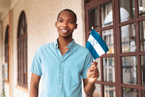 Portrait of a young african man looking at camera holding a small honduras flag.