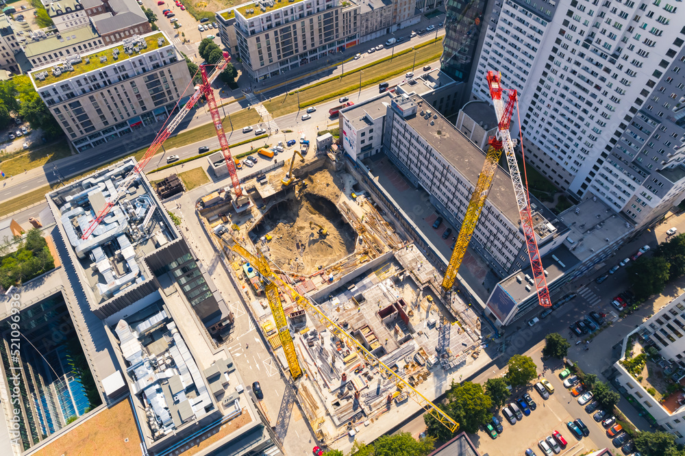 Fototapeta premium Construction workers building housing units or new skyscrapers between two buildings. Three cranes seen from aerial drone perspective. High quality photo