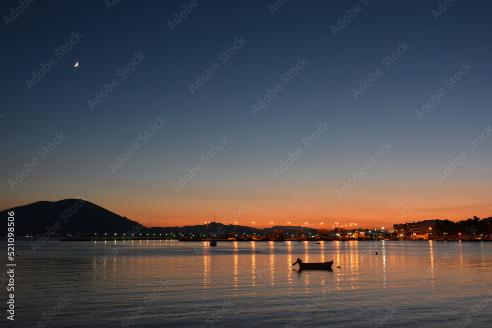 Sunset colors in the sky and reflected on the sea, with the moon and town lights at a distance. Euboea (Evia), Greece