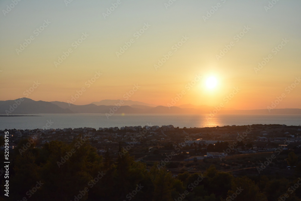 Sunset colors in the sky and reflected on the sea, with the sun and mountains at a distance. Euboea (Evia), Greece
