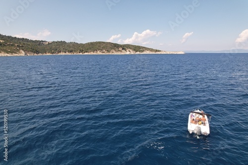 Aerial drone shot of a small white private boat moving towards an island. Cam dark-blue sea. Kolopos Agiou Oros view at Mount Athos. High quality photo photo